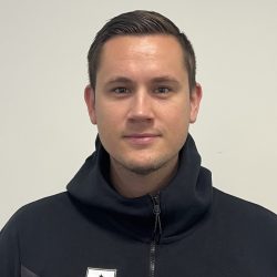 En mann med kort hår iført en svart Nike-hettegenser med en hvit logo på venstre side, poserer for et portrett mot en lys vegg. Mats Ellingsen er fanget i dette øyeblikket.
