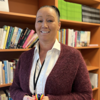 Smilende kvinne holder fargerike tusjer i en bibliotekomgivelse, og utstråler varme og lidenskap for læring eller undervisning.